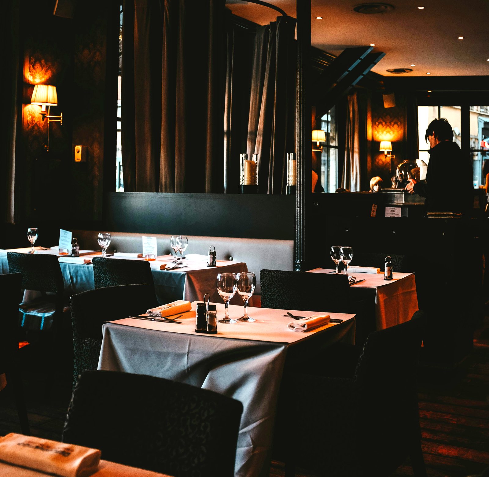 A warm, dimly lit fine-dining room with white tablecloths, wine glasses set, and low lamplight - the kind of evening room both Aspen and Vail do well
