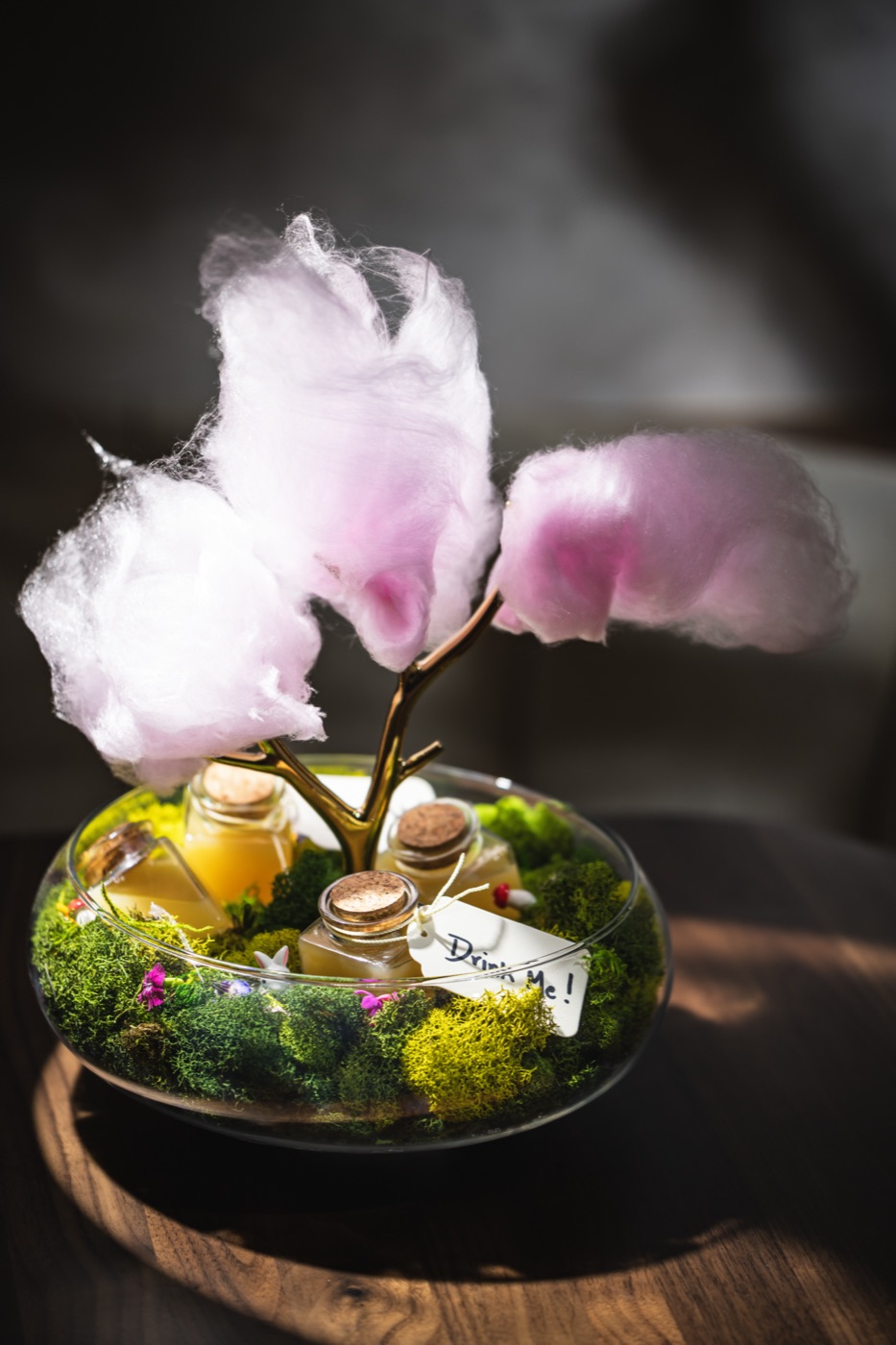 The Tulgey Woods cocktail: small bottles in a glass bowl of moss under a tree of pink cotton candy