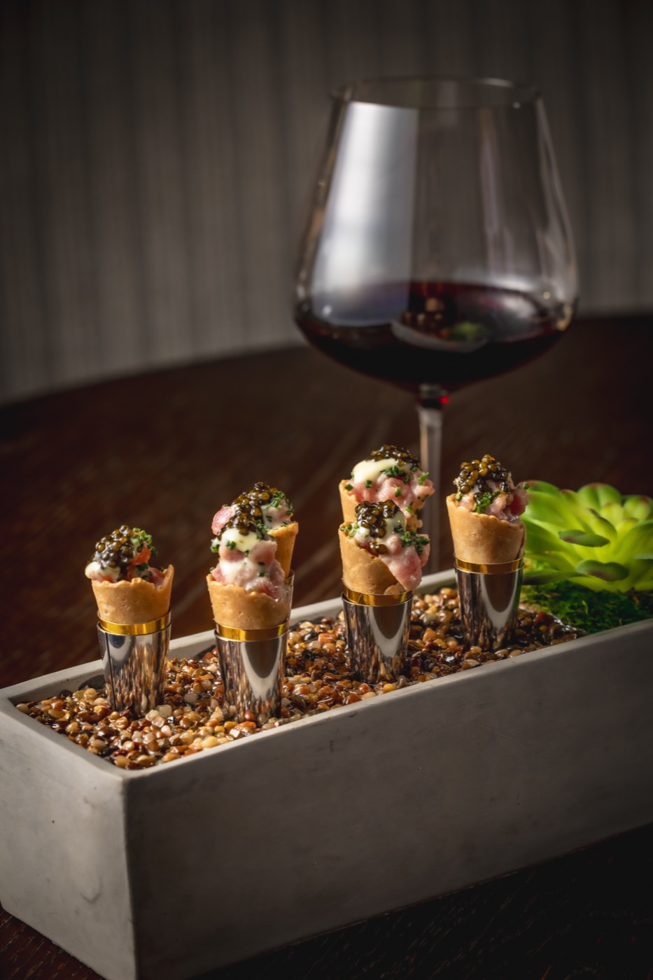 Tuna and caviar cones standing in a stone holder beside a glass of red wine